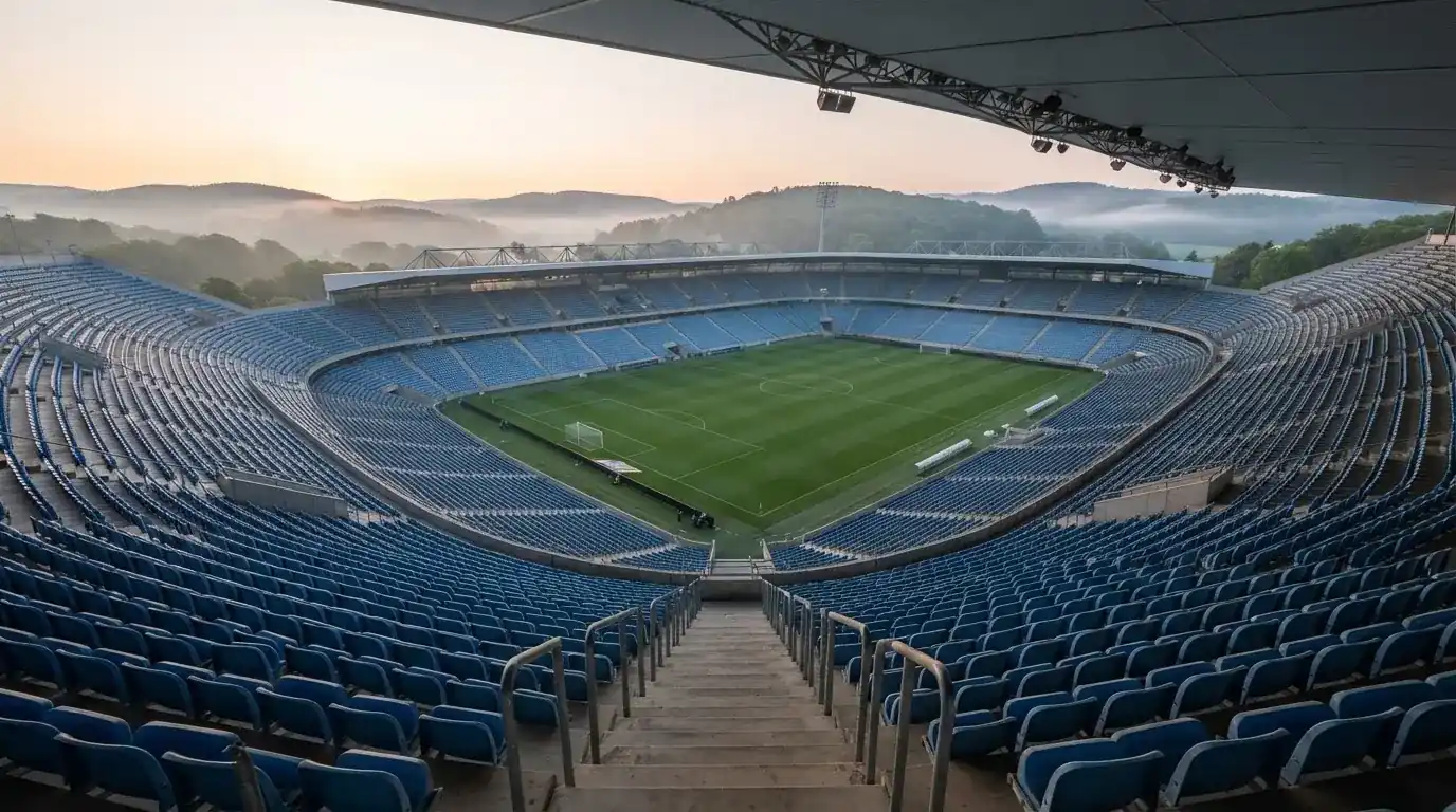 Ein leeres Stadion im Morgenlicht mit Blick auf die Sitzreihen, im Hintergrund Hügel und aufsteigender Nebel.