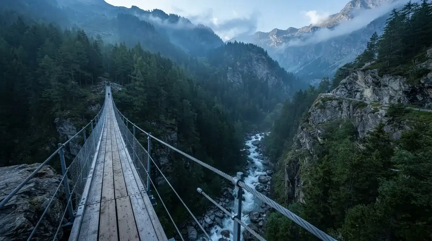 Eine Hängebrücke spannt sich über eine tiefe Schlucht, unten rauscht ein Fluss zwischen bewaldeten Felswänden.