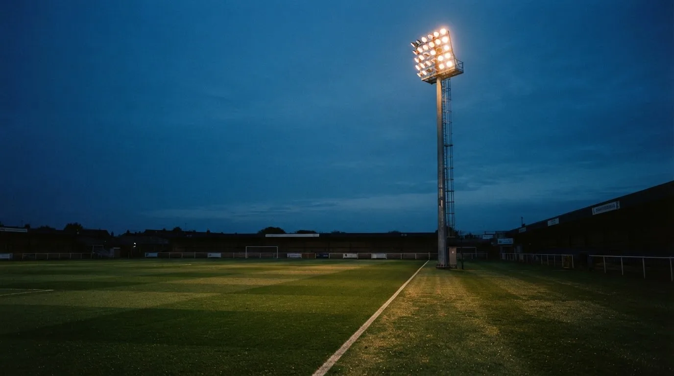 Ein Flutlichtmast ragt in den Abendhimmel, die Rasenfläche darunter liegt leer und dunkelgrün da.