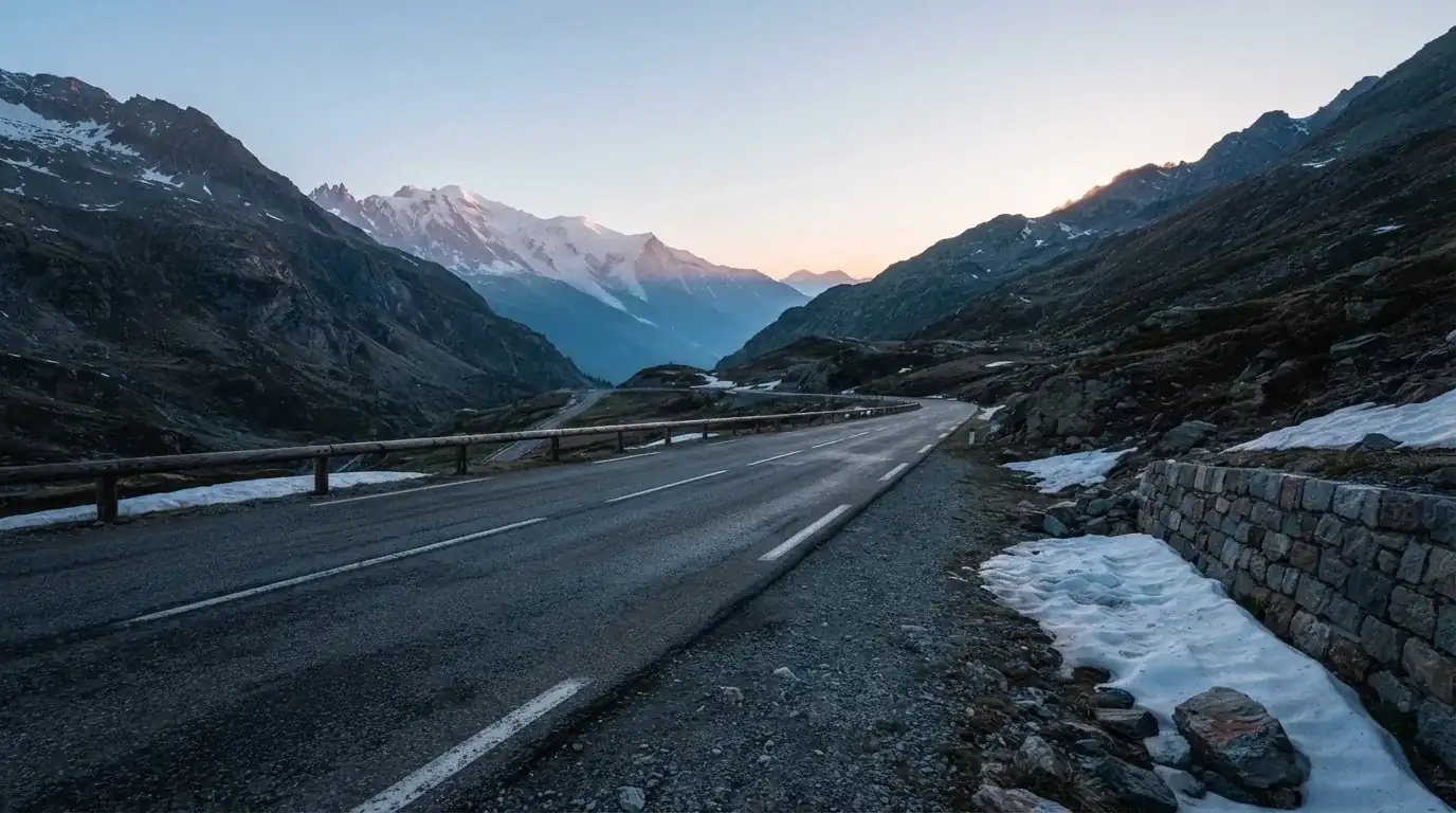 Ein Bergpass in den Schweizer Alpen mit leerer Strasse und Schneeresten am Rand im ersten Frühlicht.